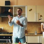 Attractive loving couple having fun in the kitchen. Handsome man juggle with apples to impress his girlfriend at home