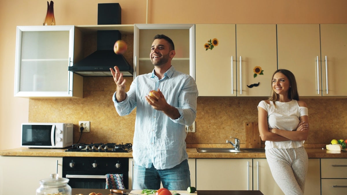 Attractive loving couple having fun in the kitchen. Handsome man juggle with apples to impress his girlfriend at home